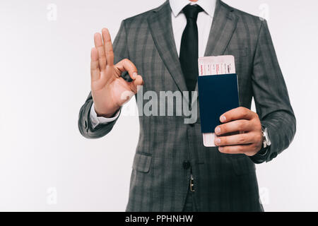 Immagine ritagliata di imprenditore tenendo il passaporto e il biglietto e che illustra bene gesto isolato su bianco Foto Stock