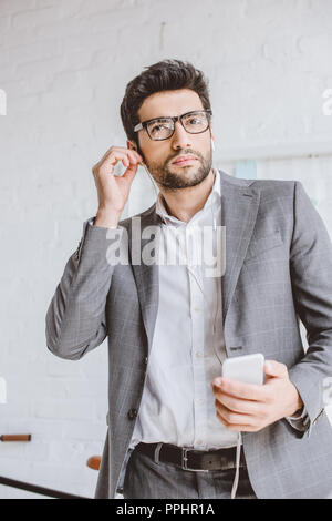 Bello imprenditore collegando gli auricolari per ascoltare la musica in ufficio Foto Stock