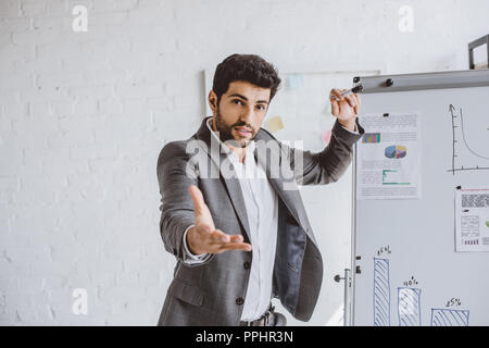 Bello imprenditore gesticolando durante la presentazione progetto sulla lavagna a fogli mobili in office Foto Stock