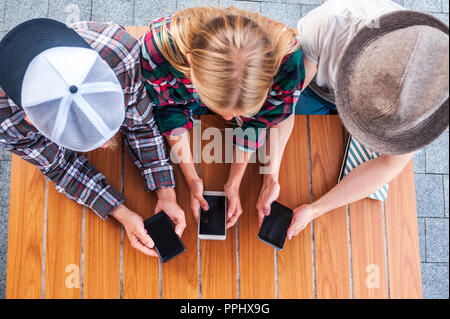 Vista aerea di giovani amici utilizzando gli smartphone con schermi vuoti al tavolo di legno Foto Stock