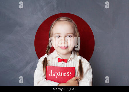 Felice bambino intelligente ragazza con libro sulla bandiera del Giappone sfondo. Apprendimento della lingua giapponese Foto Stock