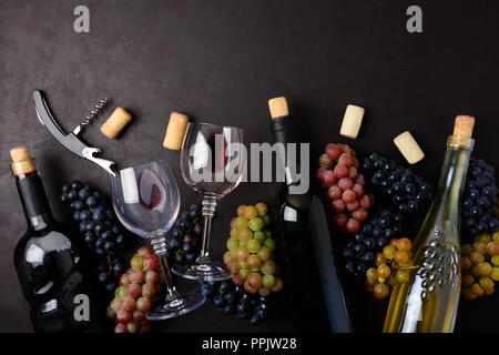 Wineglasses con vino rosso e bianco, bottiglie, uva, corkcrew e tappi giacente sul legno scuro dello sfondo. Vista dall'alto. Lay piatto. Spazio di copia Foto Stock