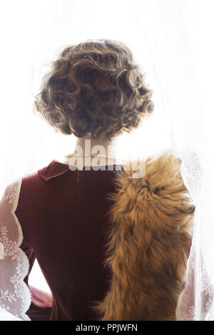 Negli anni quaranta anni cinquanta retro vintage donna in piedi dalla finestra con le tende Foto Stock
