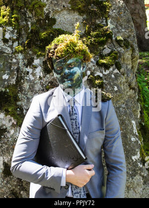 Lavoratore di ufficio in un business suit, all'aperto con un make-up sul suo volto e muschio verde sulla sua testa. L'uomo si fonde con la natura Foto Stock