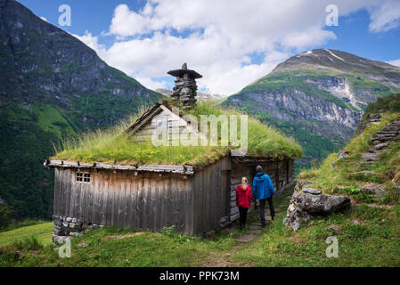 Kagefla - masi di montagna con turf case lungo il fiordo Geirangerfjorden. Attrazione turistica della Norvegia. Una coppia di viaggiatori che visitano Sca tradizionali Foto Stock