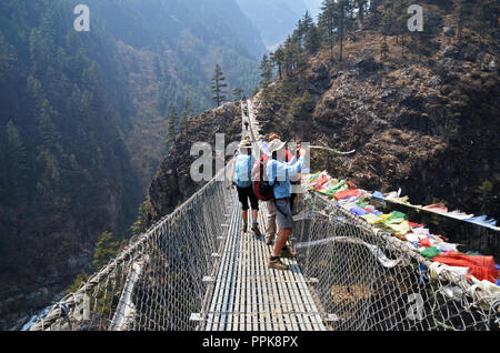 Un escursionista si ferma per una foto mentre attraversa un ponte sospeso vicino alla confluenza dei fiumi Dudh Kosi e Bhote Kosi, sotto Namche Bazaar, Nepal Foto Stock