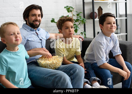 Uomo sorridente e un po' di figli con popcorn guardando film insieme a casa Foto Stock