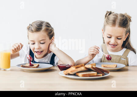 Felice Piccole sorelle di mangiare pane tostato con marmellata per colazione isolato su bianco Foto Stock