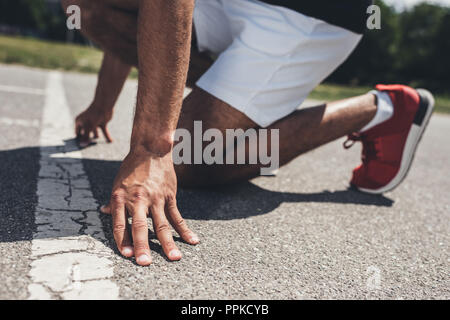 Immagine ritagliata del velocista maschio nella posizione iniziale sulla via di corsa Foto Stock