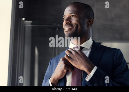 Sorridente giovane imprenditore a mettere su il suo tirante in bagno e guardando lontano Foto Stock