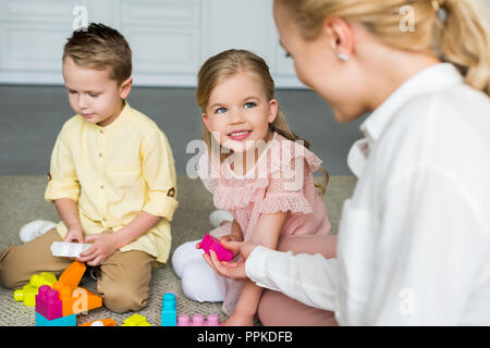 Ritagliato colpo di madre guardando carino ci sono bambini che giocano con i blocchi colorati a casa Foto Stock