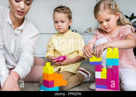 Ritagliato colpo di madre con graziosi ci sono bambini che giocano con i blocchi colorati a casa Foto Stock