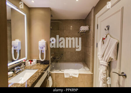 Doccia, bagno in hotel - Accessori per il bagno, asciugacapelli, specchio sopra il lavandino e accappatoio sullo sportello, sfondo Foto Stock