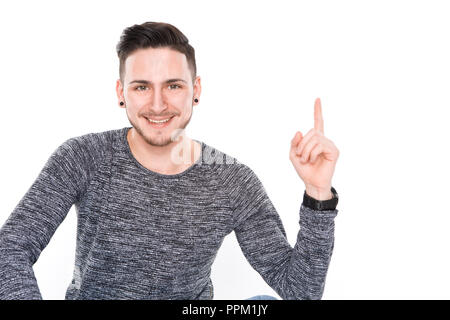 Bruna giovane uomo con sorriso sul suo volto mostra il dito fino al punto qualcosa in chiave di alta studio Sfondo bianco Foto Stock