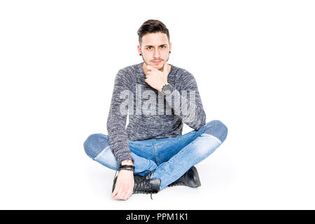 Casual bruna giovane uomo seduto sul pavimento ritratto sorridenti - isolato in uno sfondo bianco studio Foto Stock