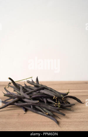 Un organico di pila di viola i fagiolini verdi su un contatore di legno Foto Stock