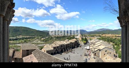 Una vista della piazza principale (Plaza Mayor) circondato da case in pietra e la vecchia torre di castello, con montagne verdi e un cielo blu, in Ainsa, Spagna Foto Stock