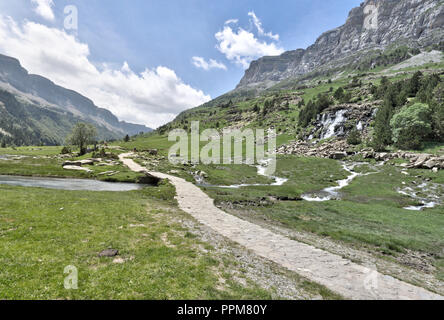 Un paesaggio di cascata e un percorso accanto al fiume Arazas, in alta montagna, pini e abeti la foresta e il cielo blu con alcune nuvole in Ordesa, Spagna Foto Stock