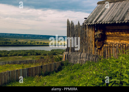 Staccionata in legno con estremità appuntite con un Log Cabin contro lo sfondo Foto Stock