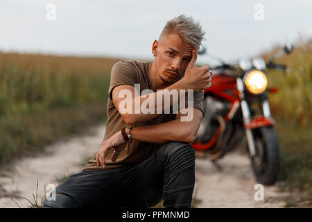 Bello di moda giovane con un'acconciatura in un elegante verde T-shirt è in sella a una motocicletta sulla natura Foto Stock