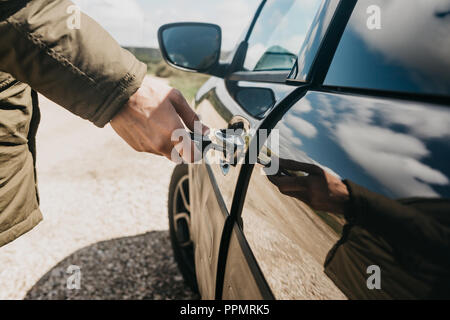 Close-up di una mano di un uomo apre la portiera della macchina con una chiave. Foto Stock