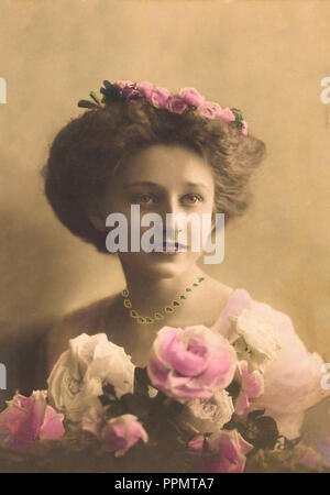 Antiquariato e Vintage donna sorridente, indossando un abito rosa e fiore di matching hat, tenendo rosa e rose bianche. Foto Stock