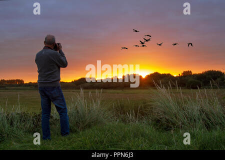 Southport, Merseyside. 27/09/2018 UK Meteo. Sunrise over Marshside Riserva naturale come un inizio di mattina fotografo registra il volo di un gregge di specie migratorie di rosa-footed oche in volo da loro posatoio per i loro terreni agricoli terreni di alimentazione. Credito; MediaWorldImages/AlamyLiveNews. Foto Stock