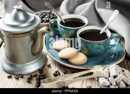 Due blue vintage tazze di caffè nero, biscotti e peltro antico caffè circondato da tela di lino, pezzi di zucchero e i chicchi di caffè sul legno vecchio Foto Stock