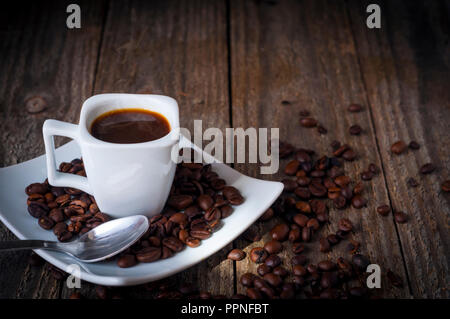 Un quadrato tazza di caffè sul vecchio tavolo in legno con fumo, alcuni grani un cucchiaio Foto Stock