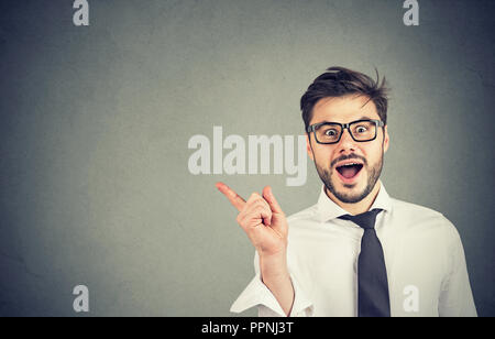 Bel giovane in bicchieri e camicia formale rivolta lontano che mostra la nuova offerta e sorridente in telecamera Foto Stock