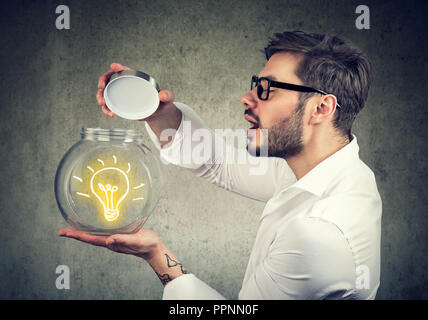 Emozionato uomo con apertura di un vasetto di vetro con brillante idea lighbulb all'interno di essere creativi Foto Stock