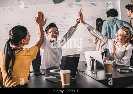 Giovane imprenditore asiatico tenendo alta cinque a femmina colleghi presso l ufficio moderno Foto Stock