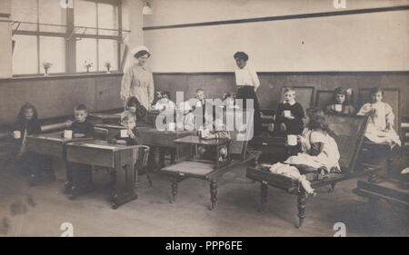 Vintage Edwardian fotografare dei bambini di bere in un aula scolastica. Insegnante e un infermiere presente. Foto Stock