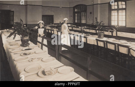 Vintage Cartolina fotografica che mostra due cameriere o il cameriere la preparazione di tabelle con stoviglie in una grande hall Foto Stock