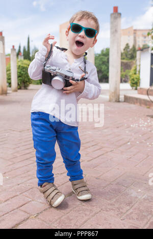 Carino felice ragazzo con foto vintage fotocamera come un po' turistico a parco. Turismo con bambini concept Foto Stock