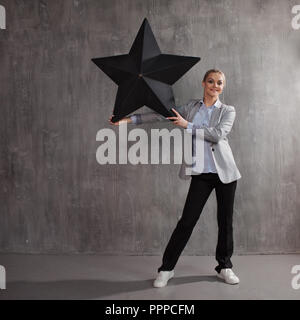 Essere una stella. Una giovane donna in un business suit con una grande stella nera in mano, concept Foto Stock