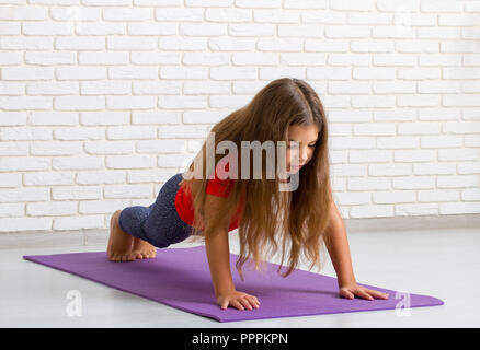 Una bambina in una sala luminosa su un tappetino palestra esegue gli esercizi sportivi e spreme al di fuori del reparto di vendita Foto Stock