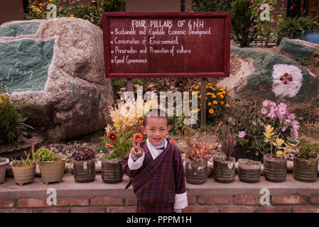 Giovani,bambino bhutanesi,nel tradizionale,Bhutan abito, volendo,in piedi,prima scuola,giardino,sulla strada per Takhtsang,Paro,Bhutan. Foto Stock