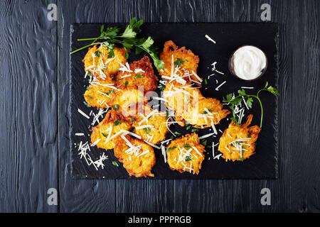 Parmesan Frittelle di zucca con panna acida, condito con prezzemolo fresco lascia sul bordo di pietra sui tavoli in legno nero , vista superiore Foto Stock