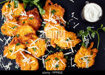 Vista superiore sulle frittelle di zucca con parmigiano grattugiato e conditi con prezzemolo tritato servito con panna acida salsa su una pietra nera di direzione su blac Foto Stock