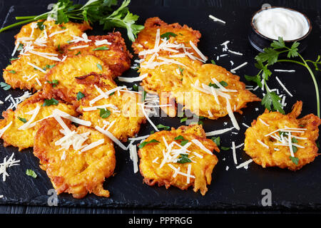 Rapido e facile da fare frittelle di zucca con shredded italiano di parmigiano e prezzemolo fresco, con panna acida salsa, servita su una lavagna nera su un nero wo Foto Stock