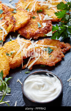 Morbido e cheesy Frittelle di zucca con panna acida e condito con prezzemolo, su una scheda di colore nero, verticale, close up Foto Stock