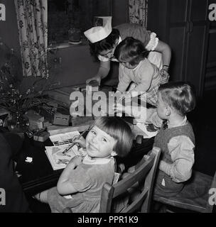 Degli anni Cinquanta, storico, post-guerra in Gran Bretagna e un infermiere aiutando tre giovani bambini che giocano con mattoni in legno e pittura in un angolo di una stanza di ospedale. Foto Stock