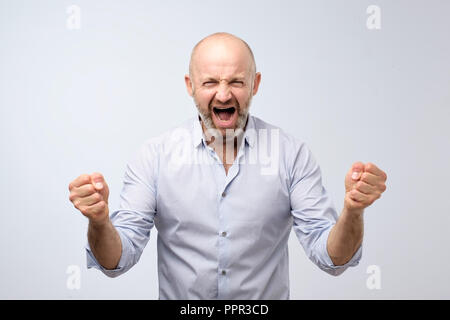 Le emozioni di una televisione ventilatore. Gridando emozionale uomo arrabbiato urlando tenendo i pugni verso l'alto. Emotiva, volto maturo. Foto Stock