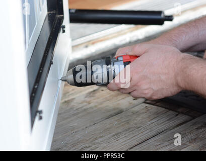 Primo piano di un uomo con le mani in mano utilizzando un utensile motorizzato per installare una porta dello schermo. Foto Stock