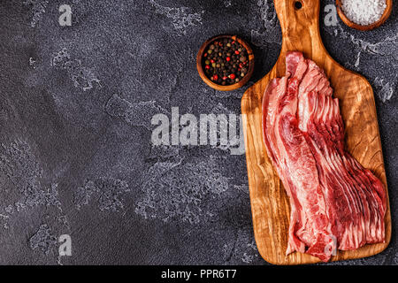 Porzione di materie Bacon strisce sullo sfondo scuro, vista dall'alto. Foto Stock