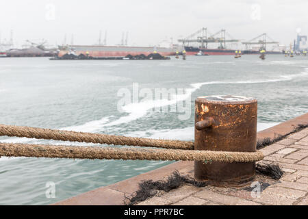 Un ferro da stiro bollard con una fune vincolata su una banchina del porto di Rotterdam nei Paesi Bassi. In background, leggermente fuori fuoco, è l'industrial sono Foto Stock