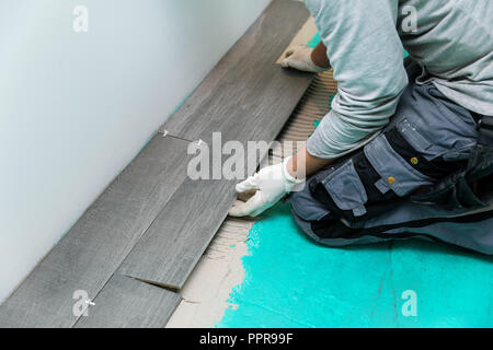 Lavoratore la posa di piastrelle per pavimento con texture di legno Foto Stock