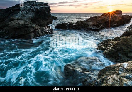 Un roccioso e aspro paesaggio costiero con il bianco delle onde che si infrangono sulla battigia e che scorre contro rocce dure in Cornwall, Regno Unito Foto Stock