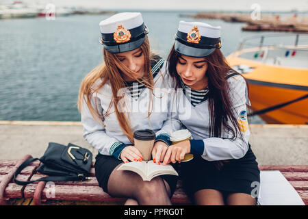 Due college studenti donne di Marine Academy la lettura di libro di mare indossando uniforme. Gli amici di studiare da costa Foto Stock